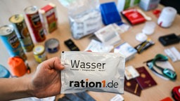 Ein Notfallpaket aus der Krisenvorsorge mit typischen Bestandteilen wie Wasser, Radio, Taschenlampe, Konserven, Erste-Hilfe-Set, Streichhölzern, Feuerzeug, Hygieneartikeln, Handschuhen, Akkus und Batterien.