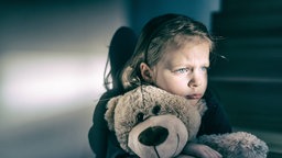 Ein Mädchen sitzt mit einem Teddybär auf einer Treppe