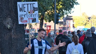 Thomas Gambling warnt mit einem Schild "Wette verloren" vor Spielsucht und Sportwetten