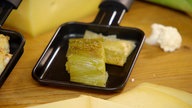 Das Bild zeigt gebackener Lauch mit kleinen Frikadellen und Raclette-Käse im Pfännchen. 