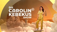 Carolin Kebekus grinst und hebt den rechte Zeigefinger gestreckt nach oben. Sie ragt aus bunten neon Leuchtringen heraus. 