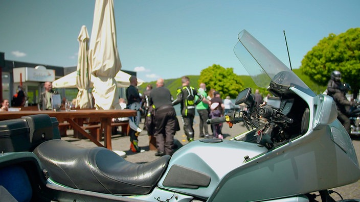 Motorradfahrer stehen an Biertischen.
