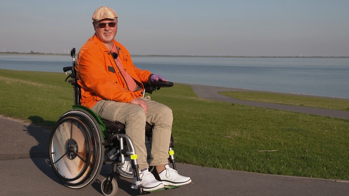 Ein Herr in einem Rollstuhl mit einer orangenen Jacke