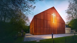Auf der Wand einer Kirche leuchtet ein Kreuz