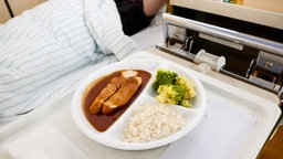 Ein Teller mit Fleisch, Reis und Romanesco auf einem Nachttisch am Krankenhausbett