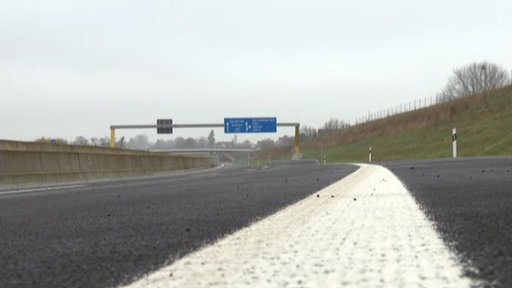 Man sieht eine weiße Fahrbahnbegrenzung auf einer Autobahn. Im Hintergrund sind Autobahnschilder zu erkennen.