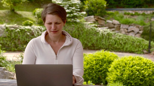 Barbara Pachl-Eberhart sitzt mit einem Laptop an einem Tisch in einem Garten.