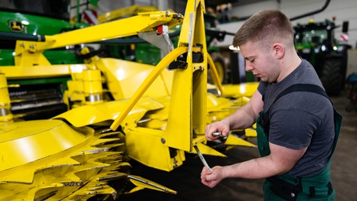 Azubi Jannis hantiert an der gelben Erntemaschine