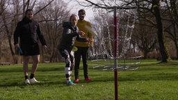 Das Bild zeigt eine Gruppe von jungen Menschen Frisbee im Park werfen.