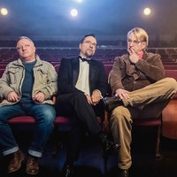 Kommissar Frank Thiel (Axel Prahl, links) und Prof. Karl-Friedrich Boerne (Jan Josef Liefers, Mitte) zusammen mit dem Mann, der in den Dschungel fiel: Die drei Männer sitzen in einem leeren Kinosaal