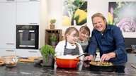 Das Bild zeigt Björn Freitag mit den zwei Kindern der Alleinerziehenden Mutter beim Kochen.