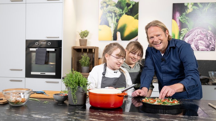 Das Bild zeigt Björn Freitag mit den zwei Kindern der Alleinerziehenden Mutter beim Kochen.