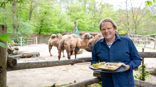 Björn Freitag steht mit einem Teller vor dem Dromedar-Gehege.