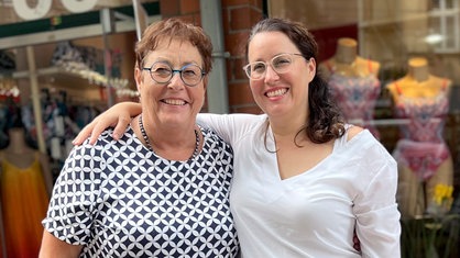 Auf dem Foto sieht man zwei Frauen, glücklich posierend vor einem Geschäft.