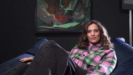 Mona Ameziane sitzt vor einem Kunstwerk
