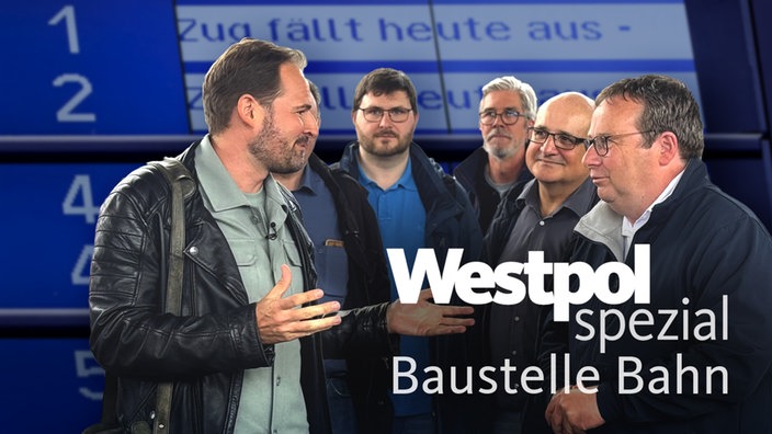 Henrik Hübschen, NRW-Verkehrsminister Oliver Krischer und Pendler*innen auf einem Bahngleis. Auf der Anzeigetafel im Hintergrund steht Zug fällt heute aus