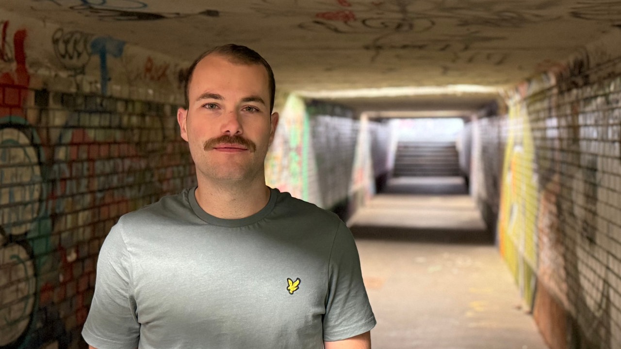 Junger Mann mit Schnurrbart schaut in die Kamera