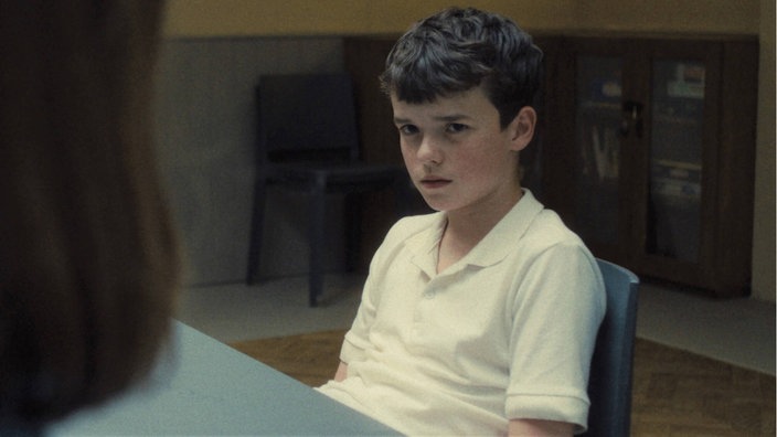Szene aus der britischen Netflix-Serie "Adolescence": Junge in weißem T-Shirt sitzt an einem Tisch