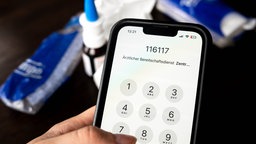 Auf einem Handy ist die Nummer des ärztlichen Bereitschaftsdienstes zu sehen 