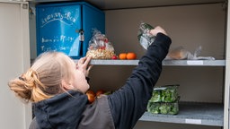 Frau greift in einen geöffneten Fairteilerschrank mit Lebensmitteln.