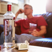 Ein Mann sitzt auf dem Sofa, vor sich eine Flasche Schnaps und Zigaretten