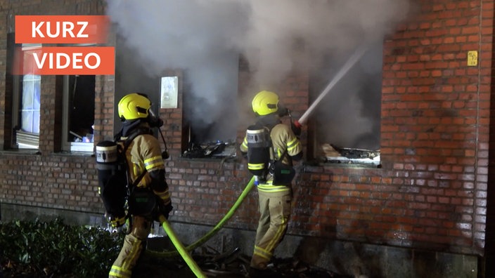 Zwei Feuerwehrleute löschen einen Brand durch das Fenster eines Hauses