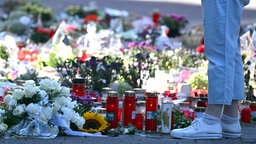 Eine Person steht vor Blumen und Kerzen, die zum Ausdruckder Trauer niedergelegt wurden