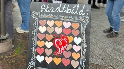 Ein Plakat mit Herzen zur Stadtbild-Debatte auf der Demonstration in Arnsberg