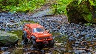 Rotes ferngesteuertes Auto fährt durch einen Bach