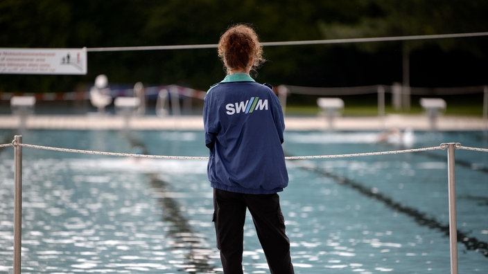 Eine Bademeisterin steht am Rand eines Schwimmbeckens.