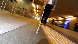 Frau mit Langstock an einem Bahnhof