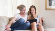Mutter und Tochter sitzen auf einem Sofa und schauen auf ein Tablet.