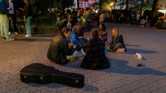 Junge Menschen sitzen mit Gitarre auf dem Boden vom Brüsseler Platz