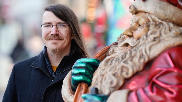Ein Mann mit Brille steht neben einer Weihnachtsmannfigur