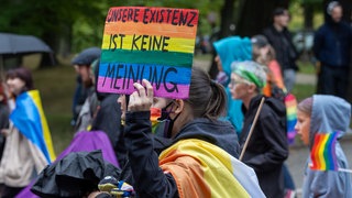 Eine Frau hält ein Schild mit der Aufschrift - UNSERE EXISTENZ IST KEINE MEINUNG - beim Umzug zum Christopher Street Day.