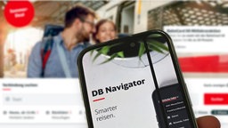 Eine Hand hält ein Handy mit der DB-App vor einem Desktop-Computer, auf dem die DB-Website geöffnet ist