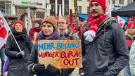 Eine Frau hält ein Schild mit der Aufschrift: "Mehr Bildung, weniger Burn Out"