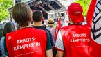 Zwei Besucher tragen Westen mit der Aufschrift "Arbeitskämpfer*in" auf dem Rücken