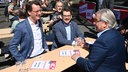 Hendrik Wüst (NRW Ministerpräsident), Thorben Albrecht (Vorsitzender des DGB Nordrhein-Westfalen) und Marc Buchholz (Oberbürgermeister in Mülheim an der Ruhr) sitzen auf einem Tisch auf der DGB Kundgebung zum 1. Mai