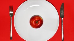 Ein Apfel liegt zum Verzehr bereit auf einem Teller