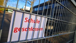 An einem Zaun ist ein Schild befestigt mit der Aufschrift: "Schule geschlossen".