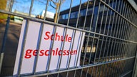 An einem Zaun ist ein Schild befestigt mit der Aufschrift: "Schule geschlossen".