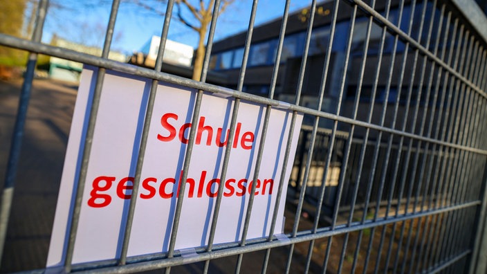 An einem Zaun ist ein Schild befestigt mit der Aufschrift: "Schule geschlossen".
