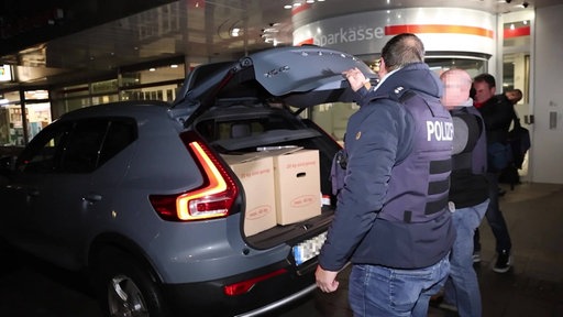 Polizeibeamte verstauen Kartons in einem Zivilfahrzeug vor der Sparkassen-Filiale in Gelsenkirchen