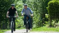 Zwei Männer auf E-Bikes fahren durch den Wald 