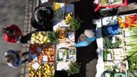 Menschen stehen an einem Marktstand mit Obst und Gemüse