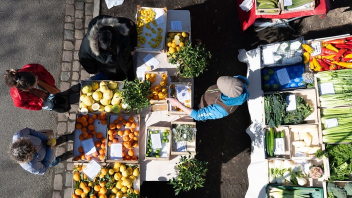 Menschen stehen an einem Marktstand mit Obst und Gemüse