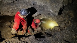 Zwei Menschen stehen mit Helmen und einer Taschenlampe zwischen Gestein