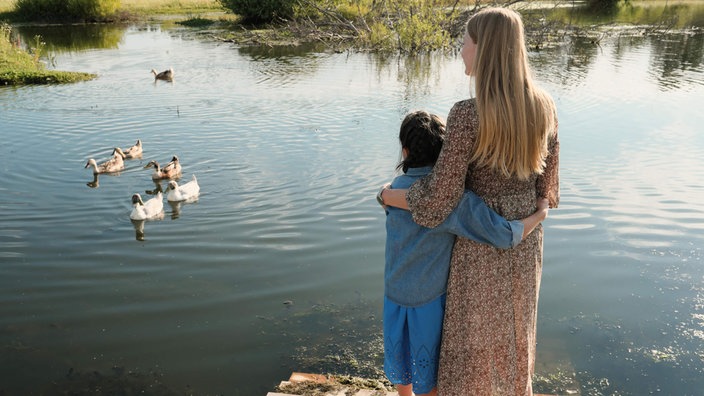 Eine Frau und ein Junge schauen sich Enten auf einem See an 