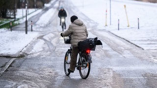  Eine Frau "schlittert" am Morgen mit ihrem Fahrrad über eine schneebedeckte glatte Straße